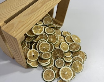 May include: A wooden crate tilted on its side, spilling out numerous dried lemon slices. The slices are circular, with a light brown center and a green rind. The crate is made of light-colored wood.