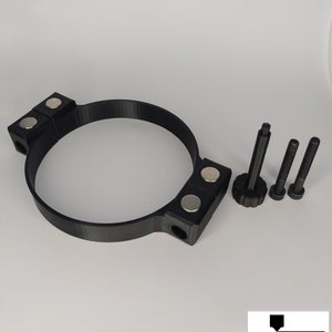 Op de afbeelding: Een zwarte, 3D-geprinte cirkelvormige beugel met twee magnetische bevestigingen en verschillende schroeven. De beugel heeft een cirkelvormig ontwerp met een diameter van ongeveer 10 cm. De schroeven zijn van verschillende lengtes en hebben een zwarte afwerking. Het logo "Wehn3D" staat rechtsonder.