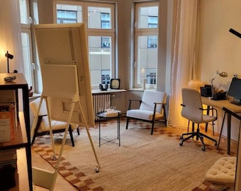 May include: A bright room with a neutral colour scheme. It features a large, off-white interactive display on a rolling stand, two white armchairs, a desk, and a patterned rug. Natural light streams in from multiple windows.