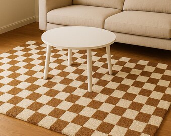 May include: A white, round coffee table with four legs sits on a brown and cream checkered rug. A beige sofa is in the background. The rug's pattern is a repeating grid of squares. The table is made of wood and has a simple design.