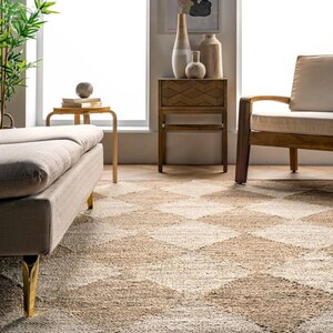 May include: A neutral-toned area rug with a geometric diamond pattern. The rug is made of natural fibers and has a textured appearance. The room also features a sofa, side table, and wooden furniture, creating a cozy living space.