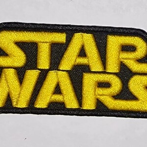 May include: A black and yellow embroidered patch with the text "STAR WARS" in a bold, blocky font.