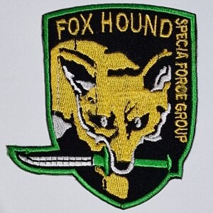 May include: A green, black, and yellow embroidered patch with a fox head and a knife. The text "FOX HOUND SPECIAL FORCE GROUP" is on the patch.