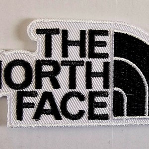 Puede incluir: Parche blanco bordado con letras negras que dicen "THE NORTH FACE" y un logotipo negro de medio domo.