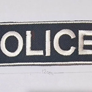 May include: A black fabric patch with white embroidered lettering that reads "POLICE". The patch is 12 inches long and 3.5 inches wide.