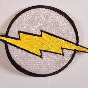 May include: A white and yellow embroidered patch with a lightning bolt design. The patch is circular and has a black outline.
