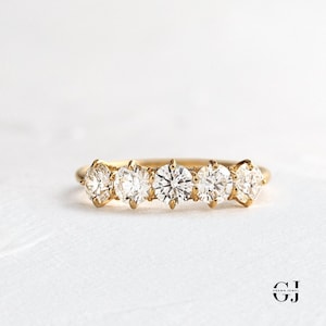 Könnte beinhalten: Ein Goldring mit fünf runden Diamanten, die in einer Reihe angeordnet sind.