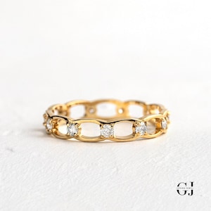 May include: A gold band ring with a delicate, openwork design featuring a row of small, clear diamonds.