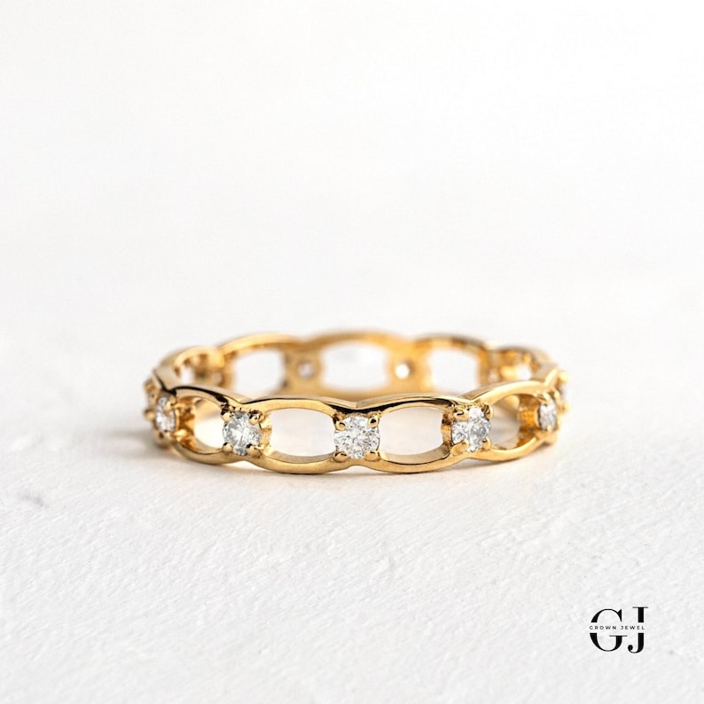 May include: A gold band ring with a delicate, openwork design featuring a row of small, clear diamonds.