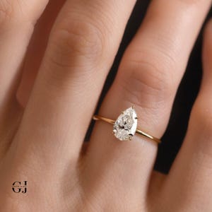 Puede incluir: Un anillo de compromiso de oro con un diamante de forma de pera. El anillo est&aacute; en un dedo.