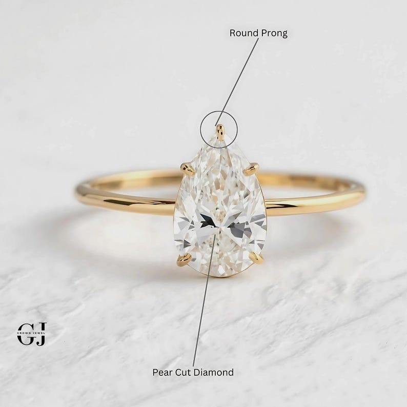 Puede incluir: Un anillo de compromiso de diamante en forma de pera con una montura de garras redondas. El anillo es de oro amarillo y presenta un diamante de talla pera.