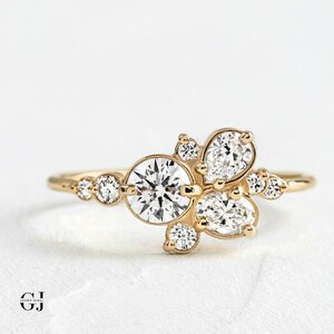 May include: A gold ring with a cluster of round and pear-shaped diamonds. The diamonds are set in a delicate, floral design.