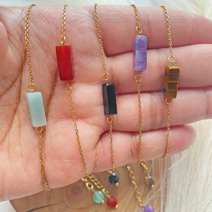May include: Five gold chain bracelets with different colored stone charms. The charms are rectangular and include green, red, black, purple, and brown stones.