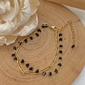 May include: A gold chain bracelet with black beads. The bracelet has a lobster clasp and an extender chain.