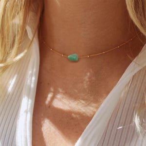 May include: A delicate gold chain necklace with a single, light green gemstone pendant.