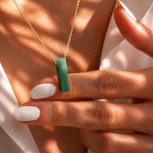 May include: A gold chain necklace featuring a rectangular, smooth, green stone pendant. The pendant is vertically oriented and suspended from a delicate gold link chain. The stone displays a solid, opaque green color with subtle variations in tone.