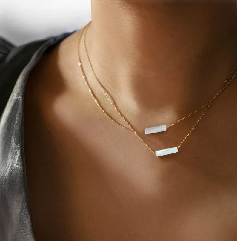 May include: A delicate gold chain necklace with two white rectangular pendants. The necklace is layered and features a simple, minimalist design.