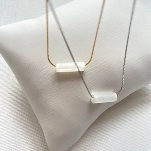 May include: Two necklaces with white rectangular stones on a white background. One necklace has a gold chain and the other has a silver chain.