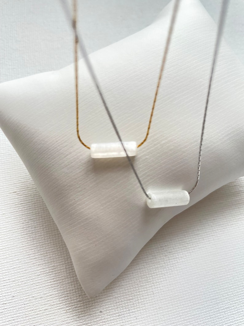 May include: Two necklaces with white rectangular stones on a white background. One necklace has a gold chain and the other has a silver chain.