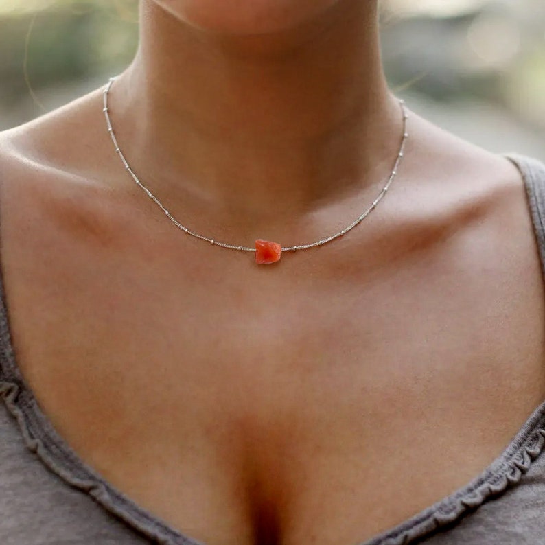 K&ouml;nnte beinhalten: Eine silberne Kettenkette mit einem kleinen, orange-roten Edelstein-Anh&auml;nger.