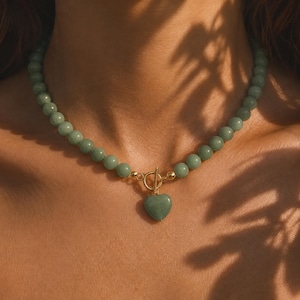 May include: A necklace featuring round, light green beads strung together, finished with a gold-toned toggle clasp. A heart-shaped pendant made of the same light green material hangs from the center of the gold-toned toggle closure.