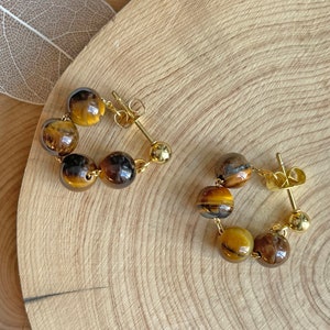 May include: A pair of gold hoop earrings with tiger's eye beads. The earrings are made of gold metal and have a simple design.