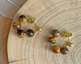May include: A pair of gold hoop earrings with tiger's eye beads. The earrings are made of gold metal and have a simple design.