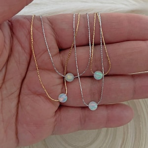 May include: Three delicate necklaces with opal beads. Each necklace features a different chain style: a gold chain, a silver chain, and a silver chain with a gold accent. The opal beads are iridescent and have a white, blue, and green color.