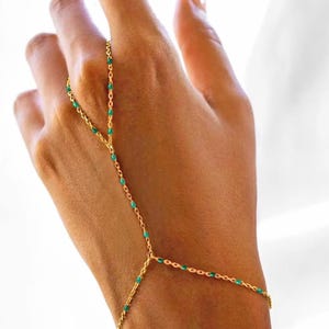 May include: A gold chain bracelet with green accents. The bracelet is designed to be worn on the wrist and finger.