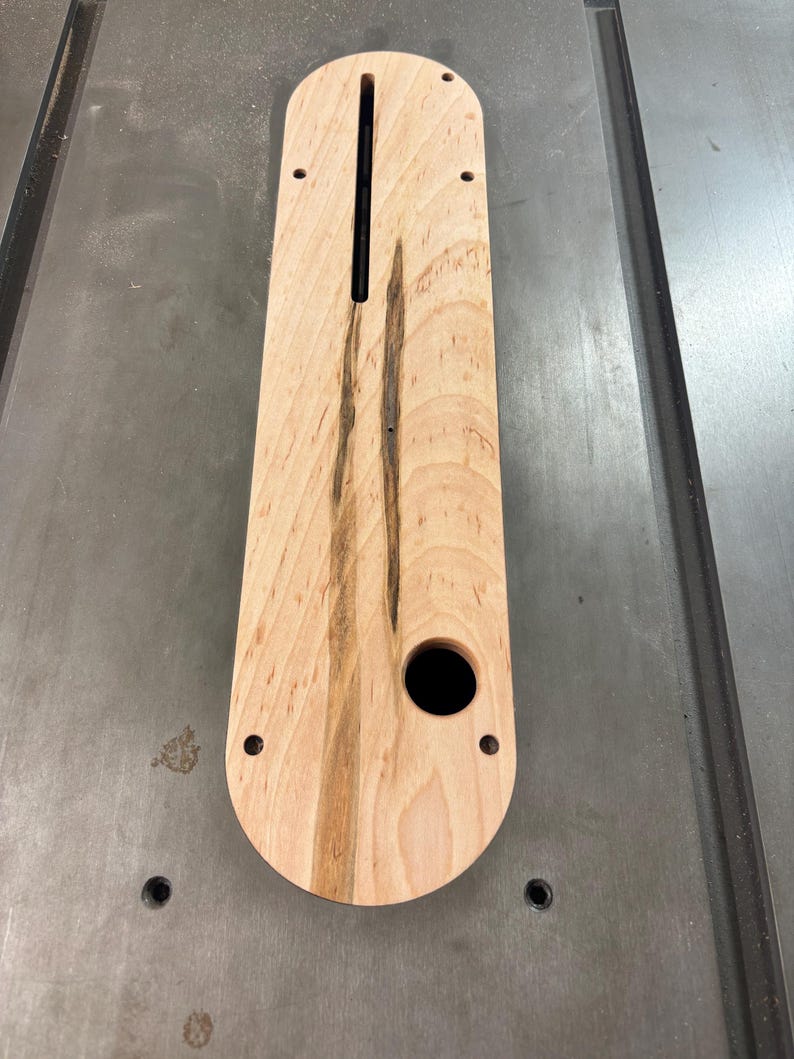 K&ouml;nnte beinhalten: Ein Holzeinsatz f&uuml;r eine Tischkreiss&auml;ge mit einer rechteckigen &Ouml;ffnung und einem runden Loch. Der Einsatz ist aus hellem Holz mit dunkelbraunen Streifen.