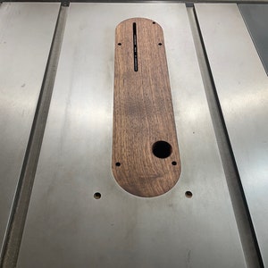 K&ouml;nnte beinhalten: Nahaufnahme einer Tischkreiss&auml;ge mit einem Holzeinsatz in der Tischfl&auml;che. Der Einsatz ist oval geformt und hat ein Loch in der Mitte. Die Tischkreiss&auml;ge ist aus Metall und hat eine silberne Oberfl&auml;che.