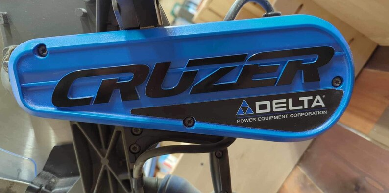 May include: Close-up of a blue and black power tool with the words "CRUZER" and "DELTA POWER EQUIPMENT CORPORATION" printed on it.