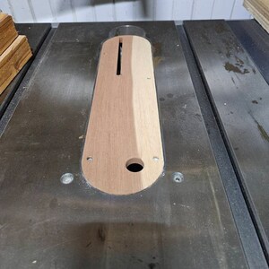 Op de afbeelding: Een close-up van een houten tafelzaag inzetstuk met een gleuf uitgesneden in het midden. Het inzetstuk is gemaakt van twee verschillende soorten hout, een licht en een donker.
