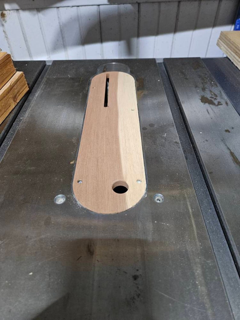 Op de afbeelding: Een close-up van een houten tafelzaag inzetstuk met een gleuf uitgesneden in het midden. Het inzetstuk is gemaakt van twee verschillende soorten hout, een licht en een donker.