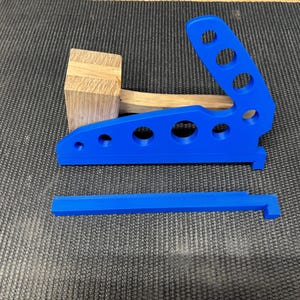 May include: A blue plastic woodworking jig with multiple holes and a lever arm. The jig is designed to help with woodworking projects.