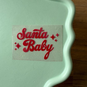 Könnte beinhalten: Ein hellgrünes Serviertablett mit gewelltem Rand und einem roten Wärmeübertragungs-Vinyl-Design mit der Aufschrift "Santa Baby" und Sternakzenten. Das Tablett besteht aus Keramik oder einem ähnlichen Material.