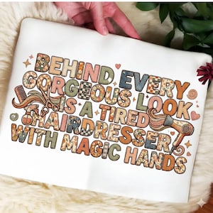 Puede incluir: Sudadera blanca con el texto "BEHIND EVERY GORGEOUS LOOK IS A TIRED HAIRDRESSER WITH MAGIC HANDS" en un diseño retro y colorido. El diseño incluye un peine, tijeras, un pulverizador y un secador de pelo.