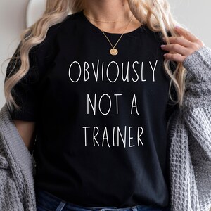 May include: Black crew neck t-shirt with the white text "OBVIOUSLY NOT A TRAINER".