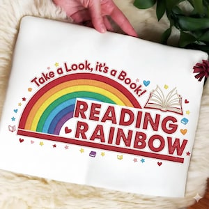 May include: White sweatshirt with a colorful rainbow design and the words "Take a Look, it's a Book!" and "Reading Rainbow" in red. The design includes hearts, stars, and an open book.