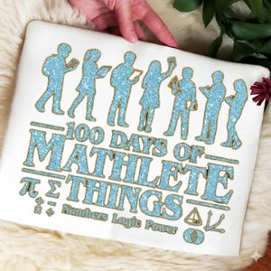 May include: White pillow with a blue glitter design featuring silhouettes of people and the text "100 Days of Mathlete Things." Includes mathematical symbols and the words "Numbers Logic Power."