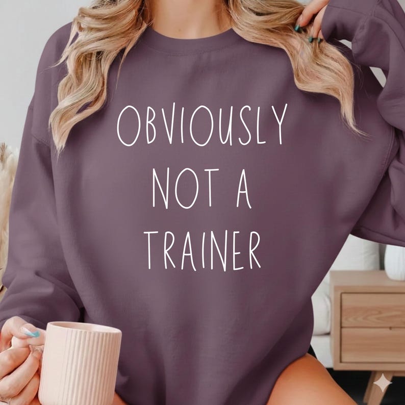 May include: A purple sweatshirt with the text "OBVIOUSLY NOT A TRAINER" in white. The sweatshirt is a solid colour and has long sleeves.