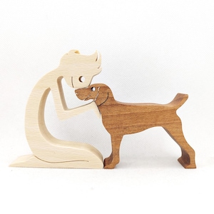 Op de afbeelding: Een houten beeldje van een persoon die knielt en naar beneden kijkt naar een hond. De persoon is gemaakt van licht hout en de hond van donker hout.
