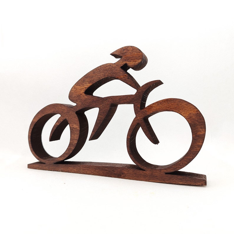Peut inclure: Sculpture en bois brun fonc&eacute; repr&eacute;sentant un cycliste sur un v&eacute;lo. Le design minimaliste montre le cycliste en position de conduite et les roues du v&eacute;lo circulaires. La sculpture est mont&eacute;e sur une base rectangulaire, faite du m&ecirc;me bois.