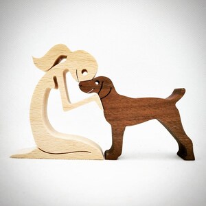 May include: Wooden figurine of a person and a dog. The person is made of light wood and is kneeling with their head bent down. The dog is made of dark wood and is standing on its hind legs with its head tilted up. The dog's head is touching the person's head.