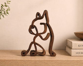 Op de afbeelding: Een donkerbruin houten sculptuur van een gestileerde dierfiguur. Het abstracte ontwerp heeft gebogen lijnen en vormen, waardoor een unieke artistieke representatie ontstaat. De sculptuur staat op een houten plank en toont zijn vorm en textuur.