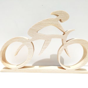 Peut inclure: Sculpture en bois clair repr&eacute;sentant un cycliste sur un v&eacute;lo. Le cycliste est en position de course, avec les roues et le cadre du v&eacute;lo clairement d&eacute;finis. La sculpture est mont&eacute;e sur une base rectangulaire.