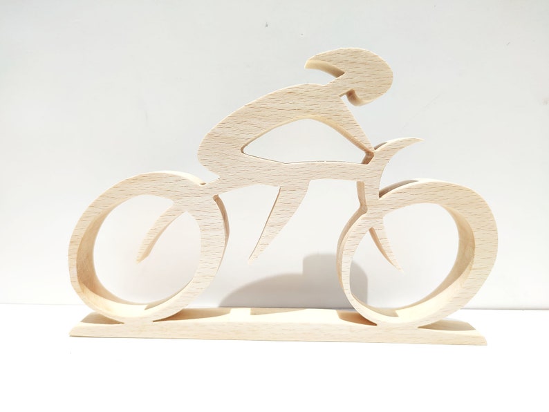 Peut inclure: Sculpture en bois clair repr&eacute;sentant un cycliste sur un v&eacute;lo. Le cycliste est en position de course, avec les roues et le cadre du v&eacute;lo clairement d&eacute;finis. La sculpture est mont&eacute;e sur une base rectangulaire.