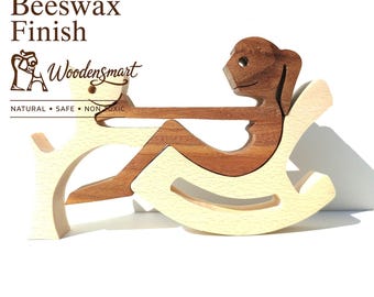 Op de afbeelding: Een houten puzzelfiguur met een donkerbruin figuur dat in een lichtbeige schommelstoel zit en interactie heeft met een lichtbeige diervorm. De tekst Natural Beeswax Finish en Woodensmart met de slogan NATURAL SAFE NON TOXIC is zichtbaar.