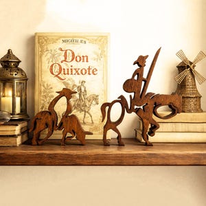 Puede incluir: Figuras de madera de Don Quijote y su caballo, junto con otros objetos decorativos, se exhiben en una estantería de madera. Un libro titulado "Don Quijote" es visible en el fondo, junto con una linterna decorativa y un pequeño molino de viento.