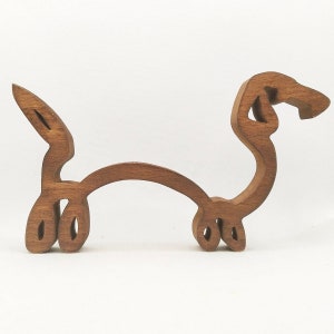 May include: A wooden dachshund sculpture, carved in a simple, abstract style. The sculpture is brown and has a smooth finish.